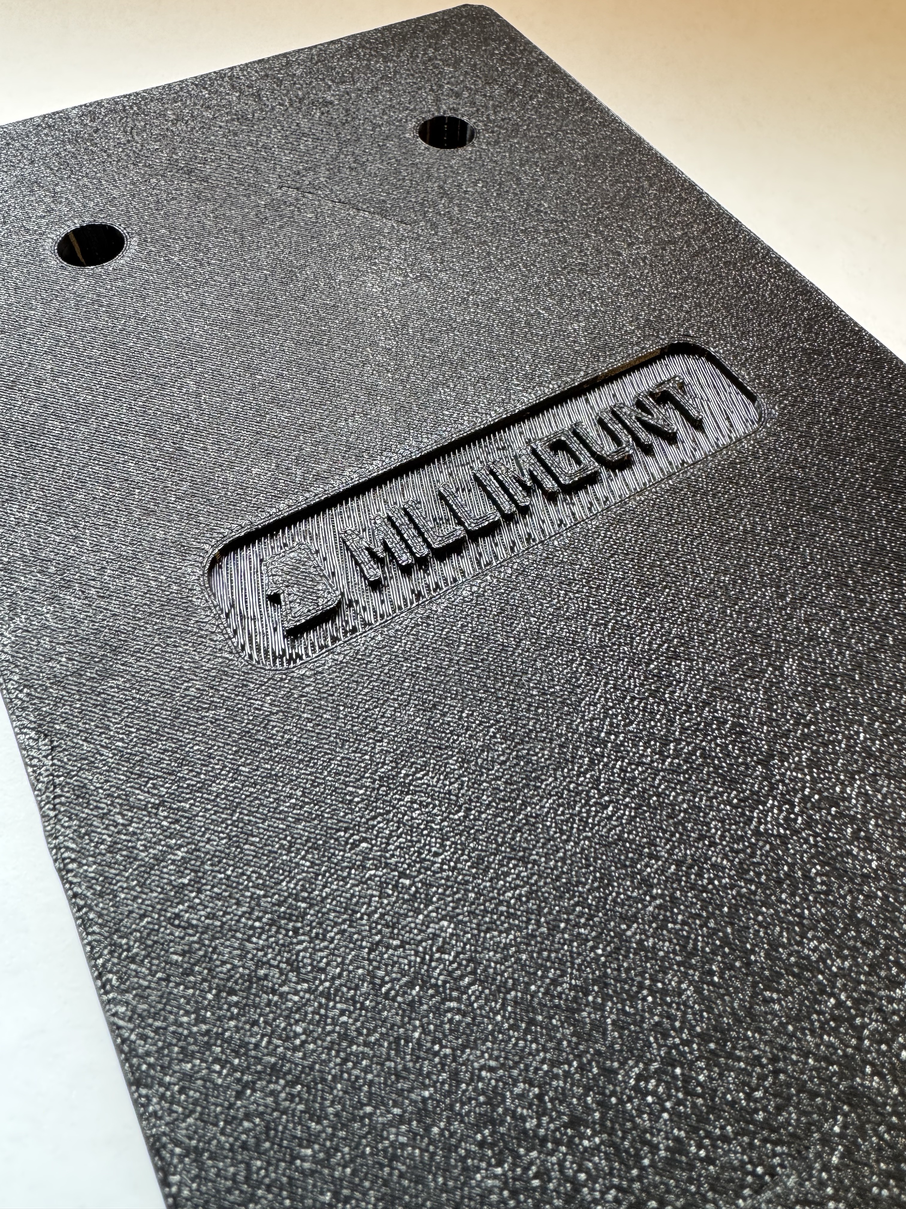 MilliMount bracket close-up showing the embossed MILLIMOUNT logo and textured surface